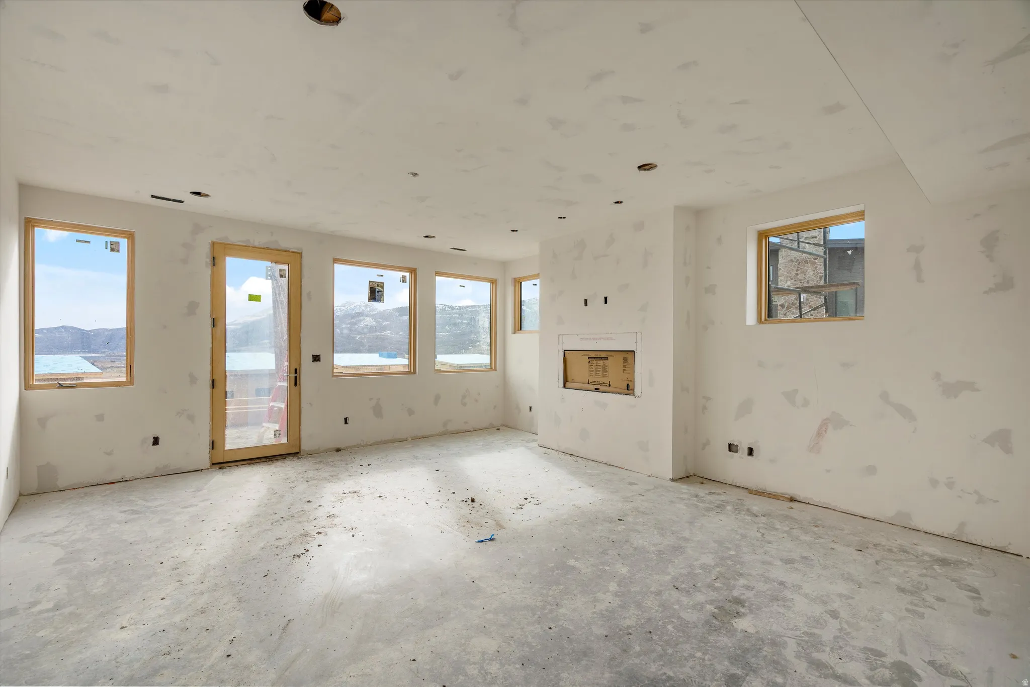 Spacious room under construction featuring multiple windows, a glass-paneled door, and a built-in fireplace opening