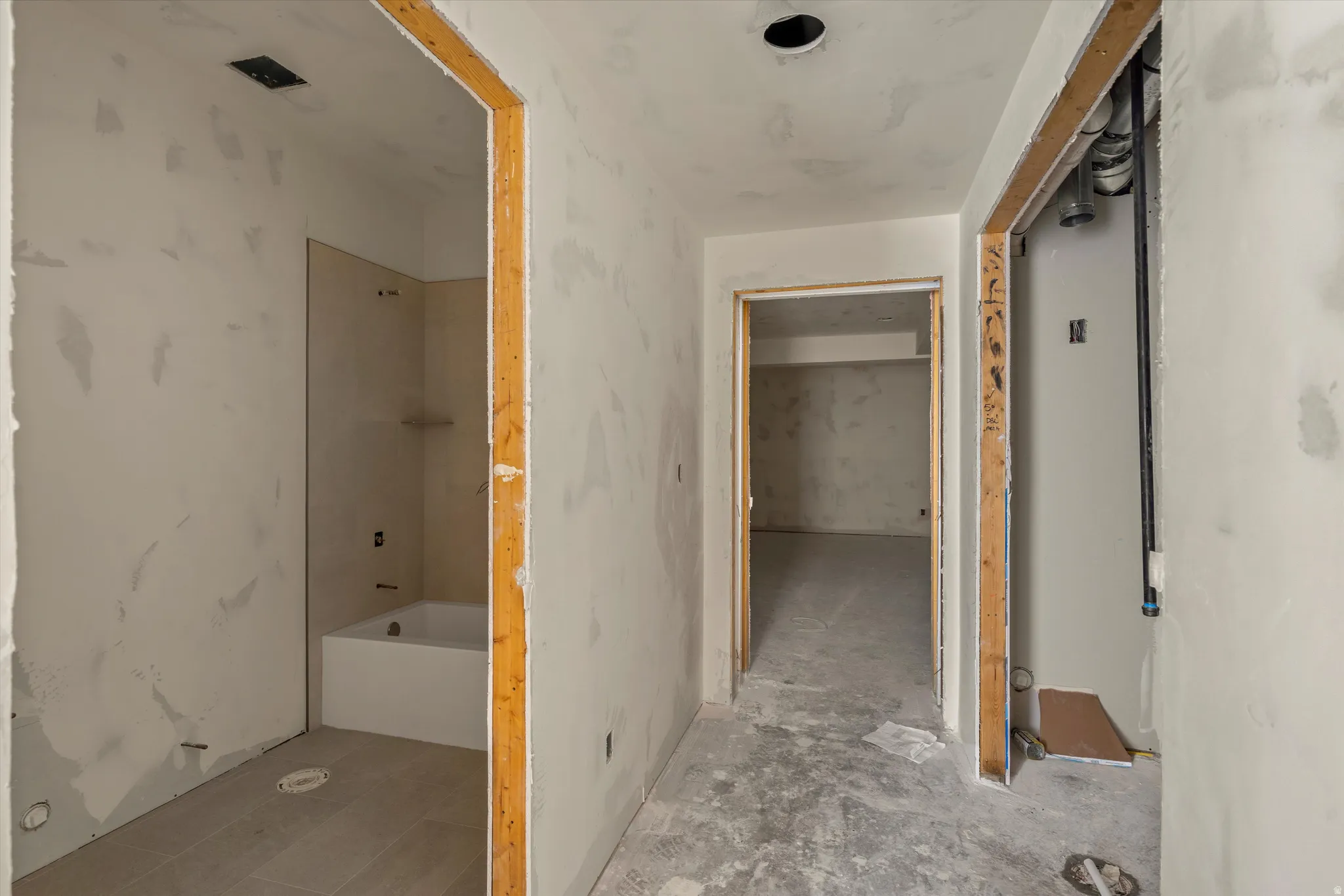 Interior hallway with exposed wood door frames, unfinished drywall, a recessed ceiling light, and concrete flooring