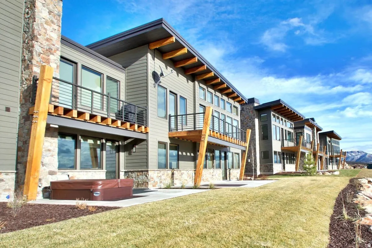 Rear view of property featuring a hot tub, stone siding, a yard, and a patio area