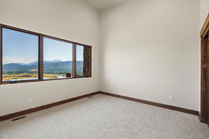 Bright corner bedroom offering expansive windows framing mountain and valley scenery, neutral carpet flooring, and wood-trimmed architectural details