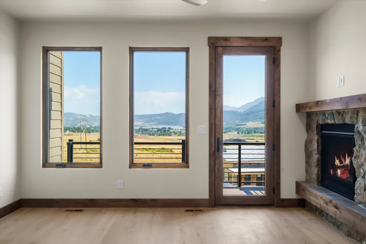 Room featuring a stone-clad fireplace with a rustic wood mantel, wood-finish flooring, two vertical windows, and a glass-paneled door with dark hardware