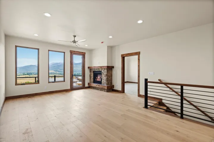 Living area featuring light wood-finish flooring, a stone-clad fireplace, and multiple windows with wooden trim
