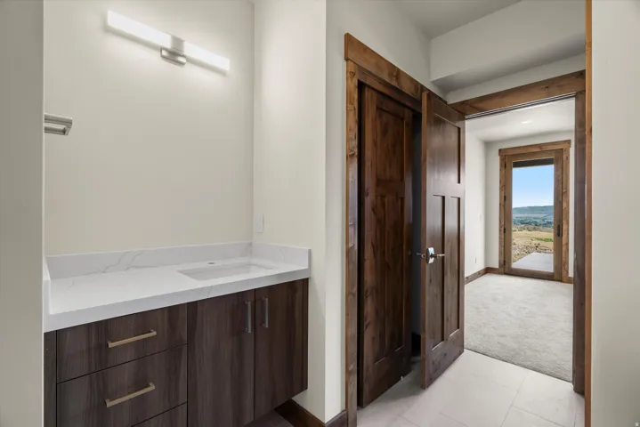 Spa-inspired primary bathroom featuring a dark wood vanity with dual sinks, white quartz countertop, chrome hardware, and linear wall sconce lighting