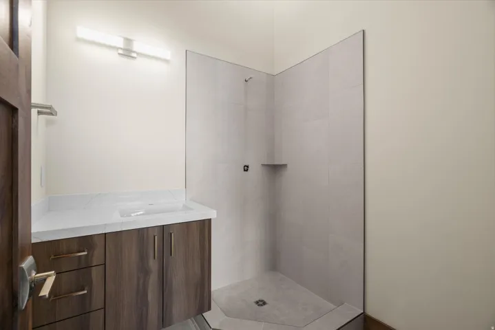 Modern bathroom featuring a wood-finish vanity with dual drawers and chrome hardware, white quartz countertop, and an integrated sink