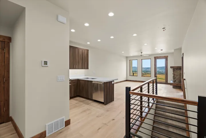 Open-concept living area with contemporary metal railing staircase, wood-finish flooring, recessed lighting, and a stone-clad fireplace
