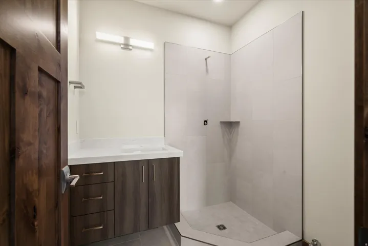 Modern primary bathroom featuring a dark wood-finish vanity with multiple storage drawers, white quartz countertop, and chrome hardware