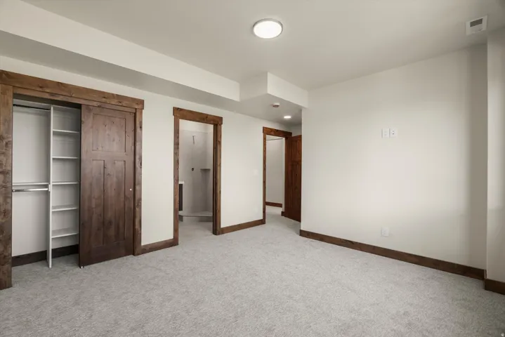 Spacious primary bedroom featuring neutral carpeting, wood-trimmed closet with sliding doors and shelving, ensuite bathroom access, and recessed ceiling lighting throughout
