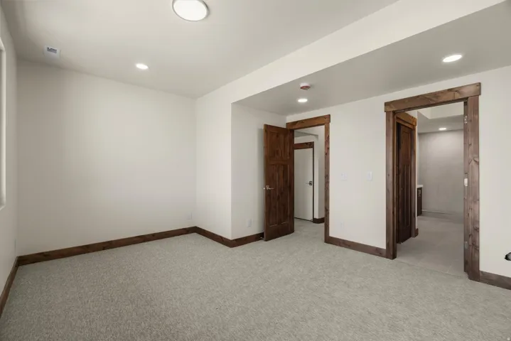 Spacious finished basement featuring neutral carpeting, recessed ceiling lighting, and multiple wood-trimmed doorways providing access to adjoining rooms