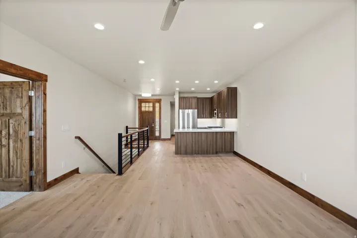 Open-concept living space featuring engineered wood-finish flooring throughout, recessed ceiling lighting, and a central staircase with black metal railing
