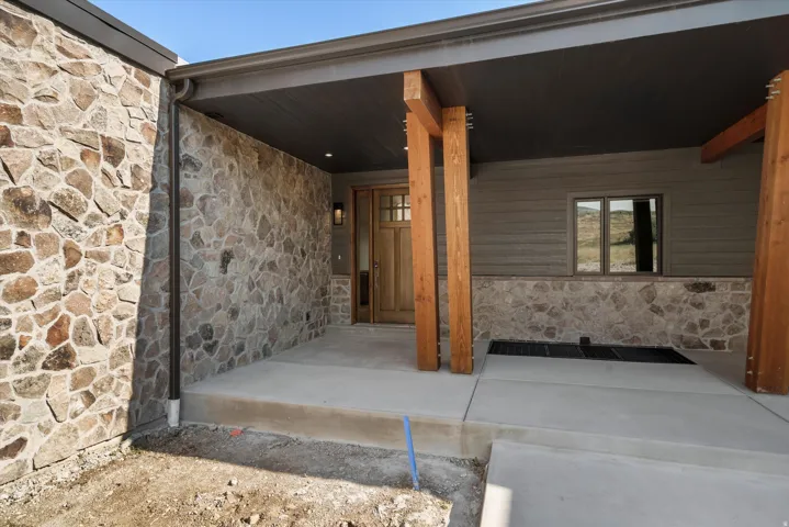 Stone veneer facade with natural wood columns, covered entry, wood-paneled door, recessed lighting, and a transom window