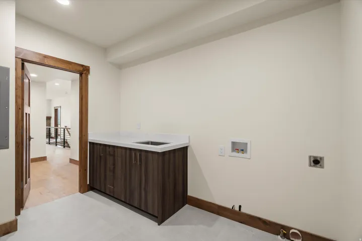 Modern utility space featuring custom dark wood-finish cabinetry with integrated countertop, recessed ceiling lighting, and finished flooring