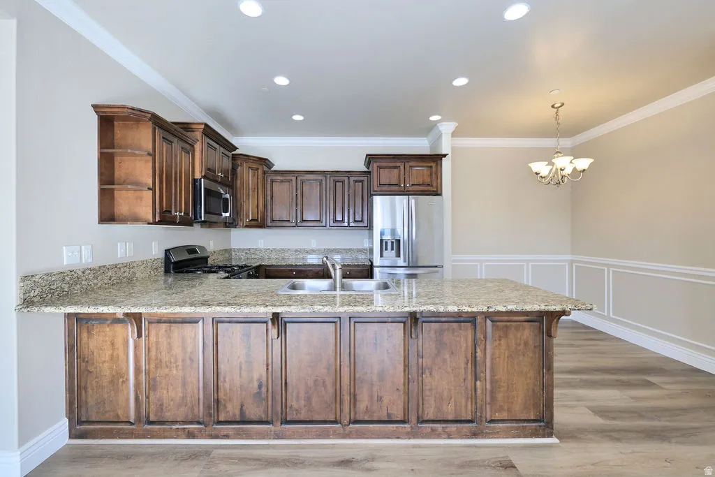 Kitchen with appliances with stainless steel finishes, a peninsula, light wood finished floors, light stone countertops, and crown molding
