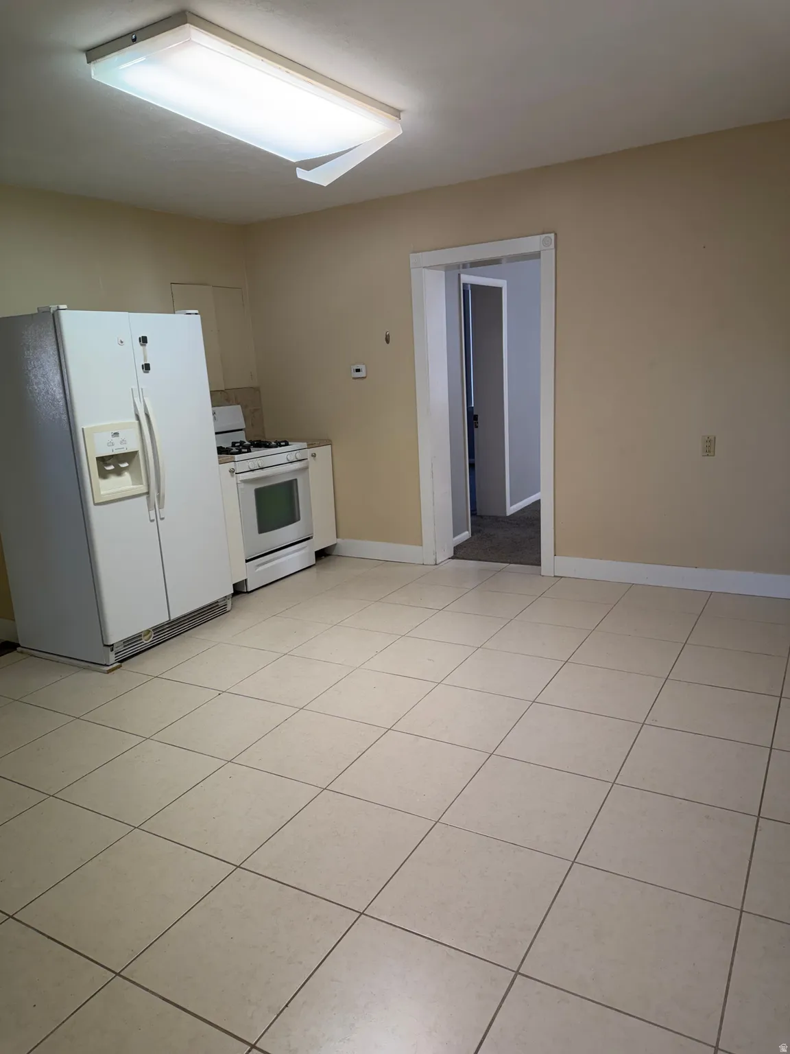 Kitchen featuring white appliances, light tile patterned floors, and white cabinets