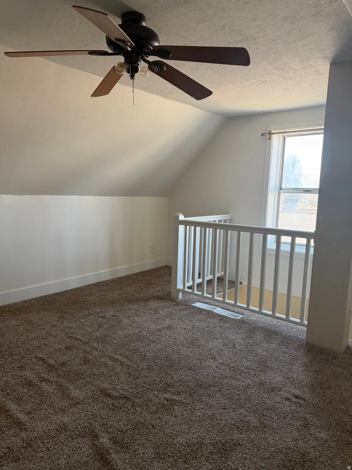 Bonus room with a textured ceiling, vaulted ceiling, dark carpet, and ceiling fan