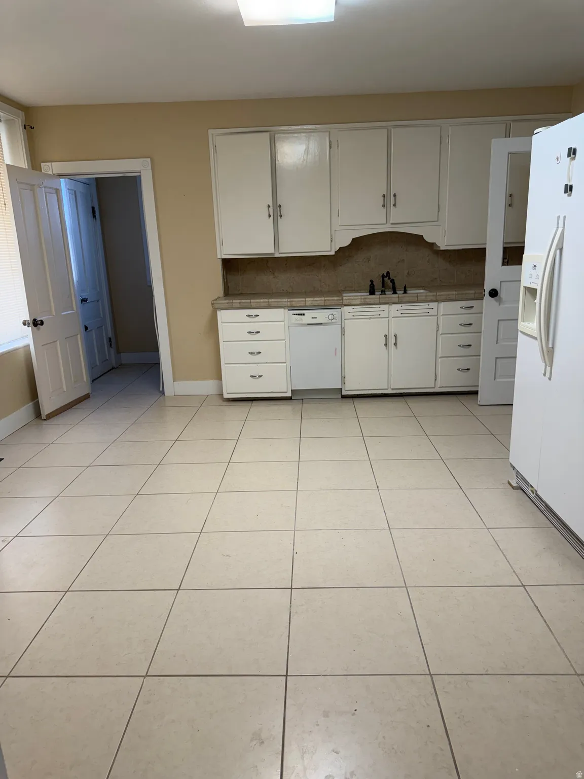 Kitchen featuring white appliances, white cabinetry, light tile patterned floors, and decorative backsplash