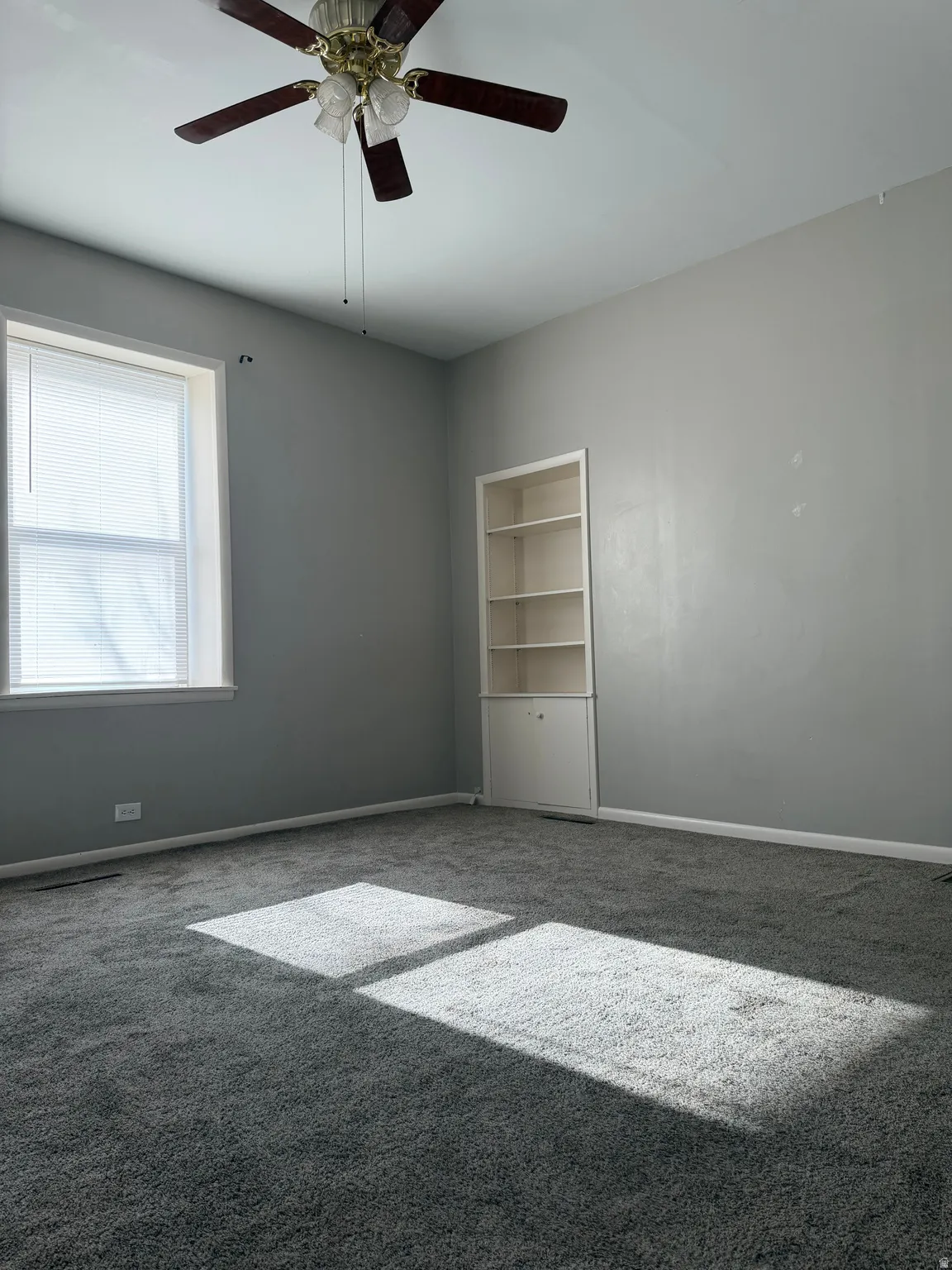 Empty room featuring carpet flooring, built in features, and ceiling fan