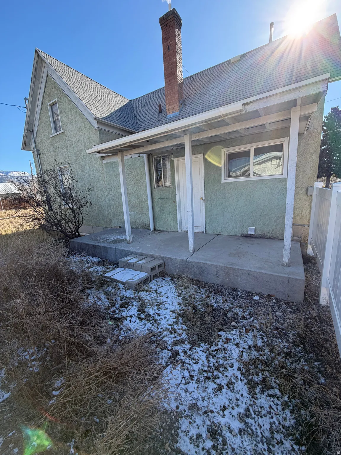 Back of house with roof with shingles, stucco siding, a chimney, and a patio area