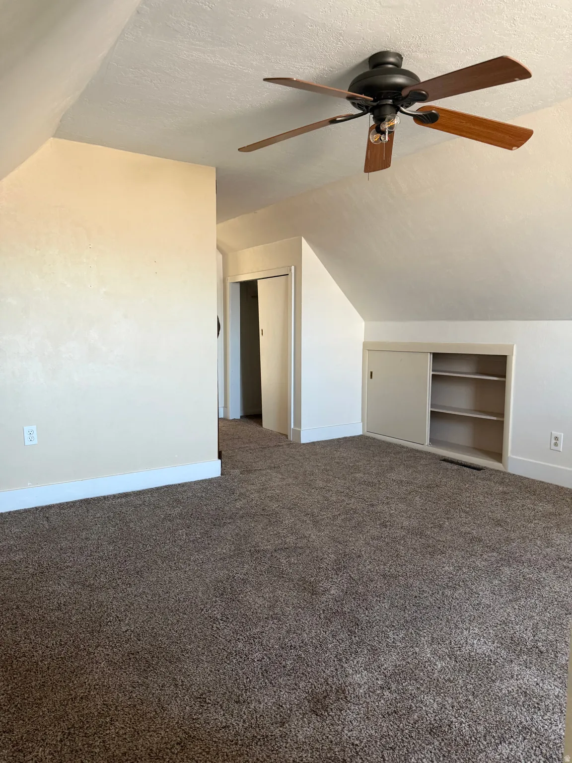 Bonus room featuring lofted ceiling, dark carpet, built in features, a textured ceiling, and ceiling fan