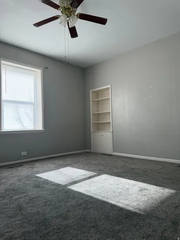 Empty room featuring carpet flooring, built in features, and ceiling fan