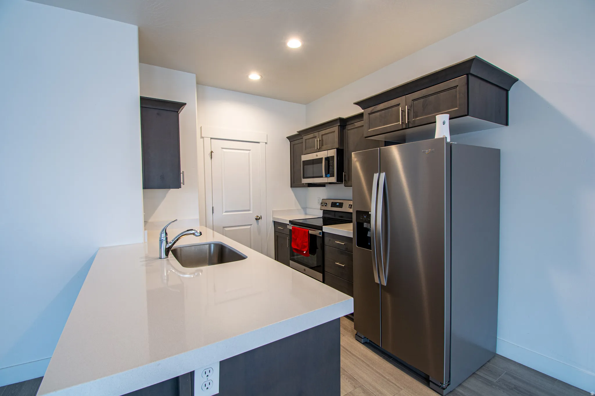 Kitchen featuring appliances with stainless steel finishes, light stone countertops, a peninsula, light wood-style flooring, and dark brown cabinets