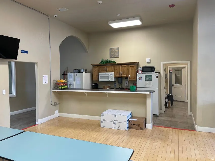 Kitchen with white appliances, a breakfast bar, a peninsula, brown cabinets, and a towering ceiling