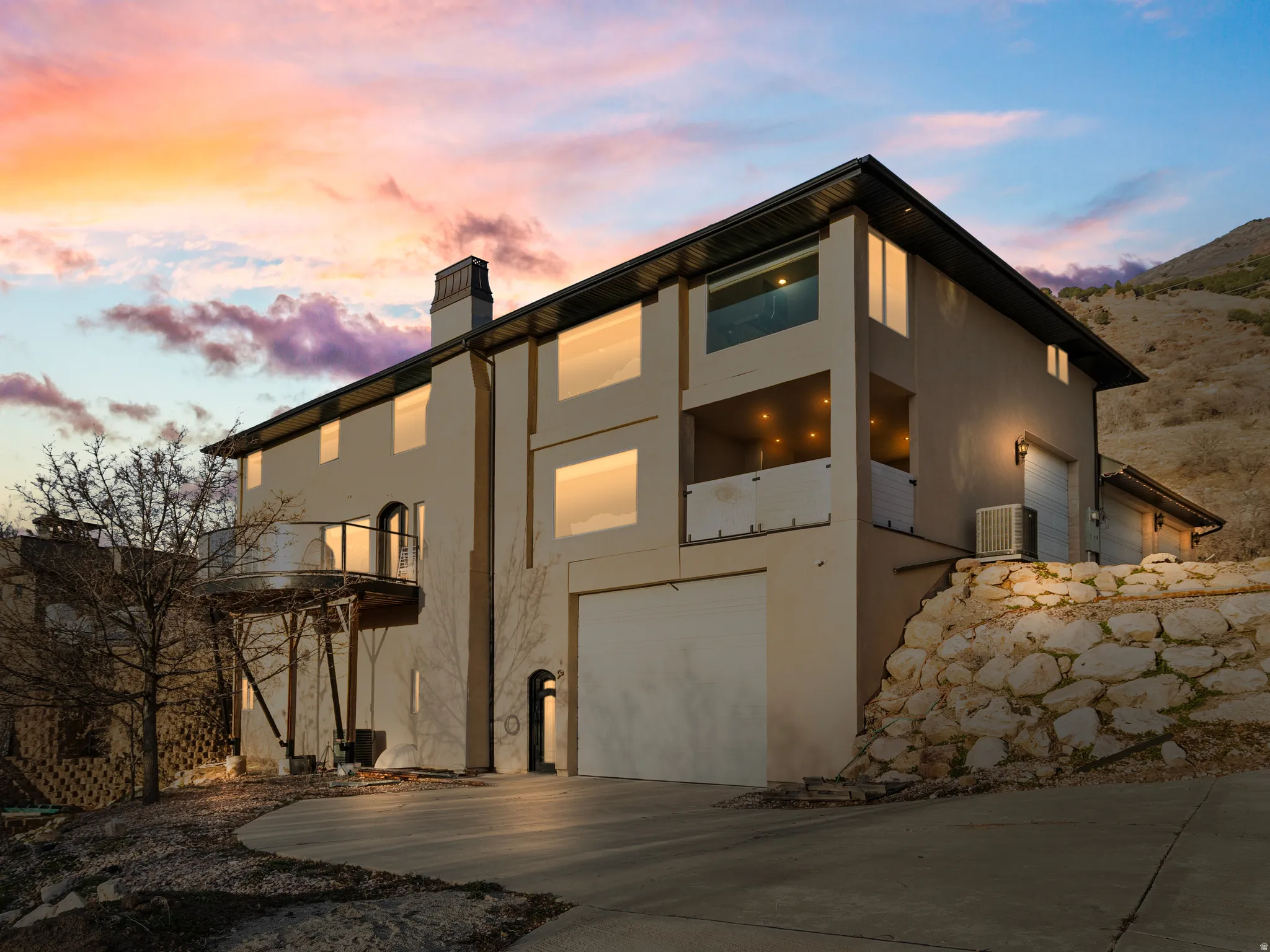 View of front of home featuring a balcony, driveway, a chimney, stucco siding, and a garage