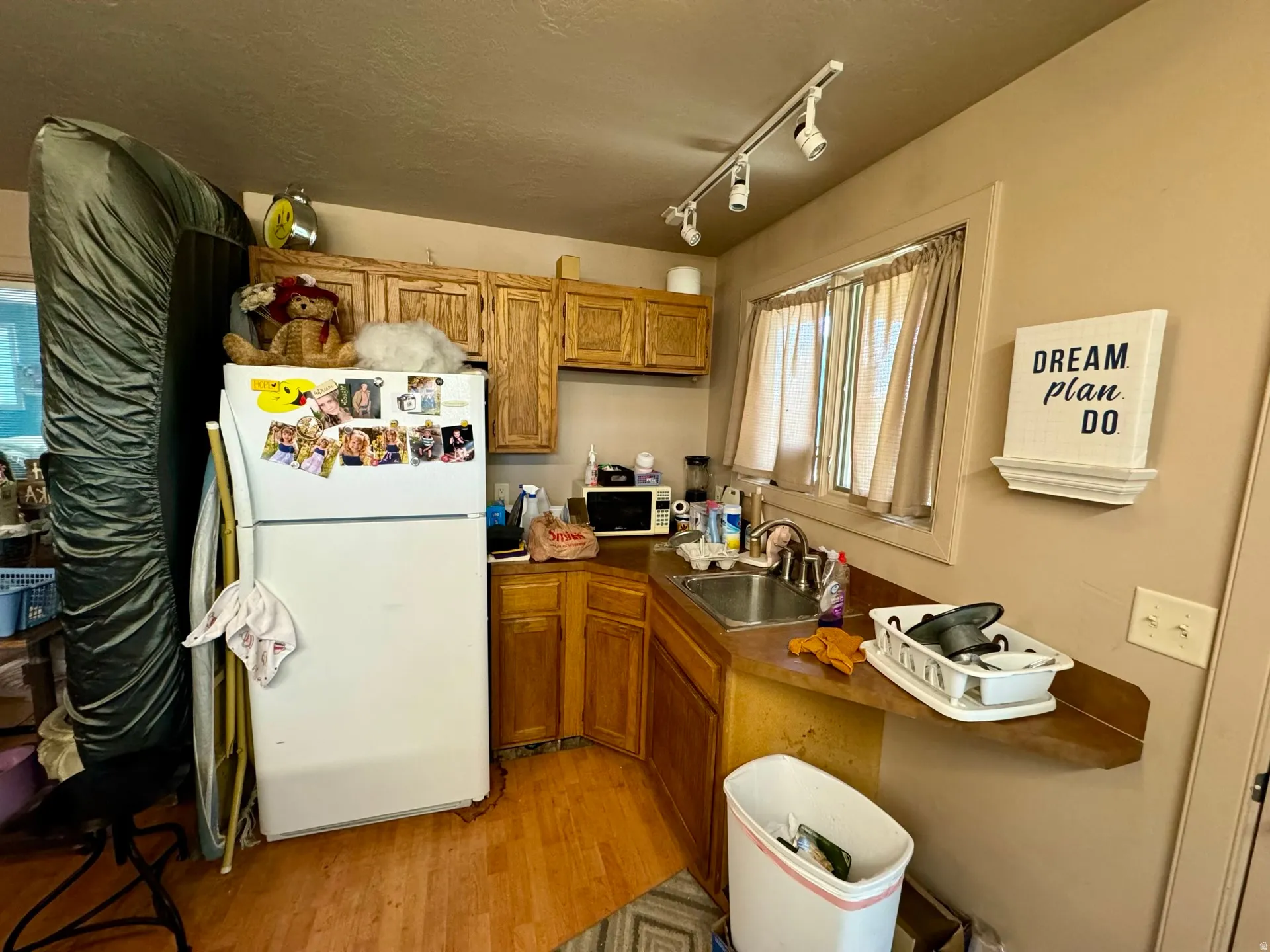 Kitchen with brown cabinetry, white appliances, light wood finished floors, track lighting, and a textured ceiling