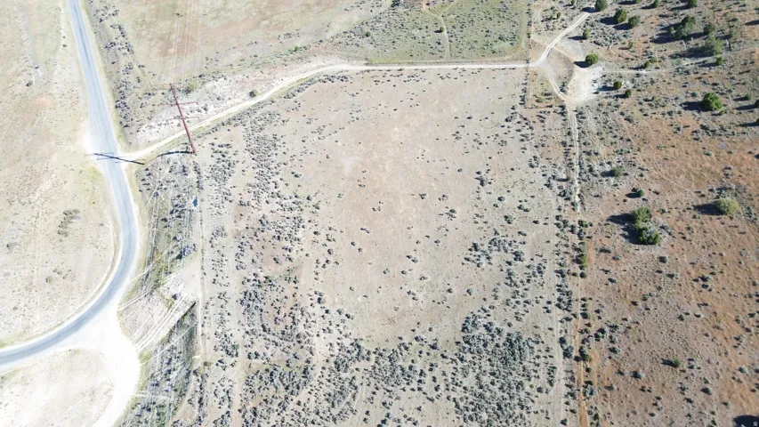 Expansive undeveloped land featuring a paved road frontage, established dirt tracks, and scattered natural vegetation
