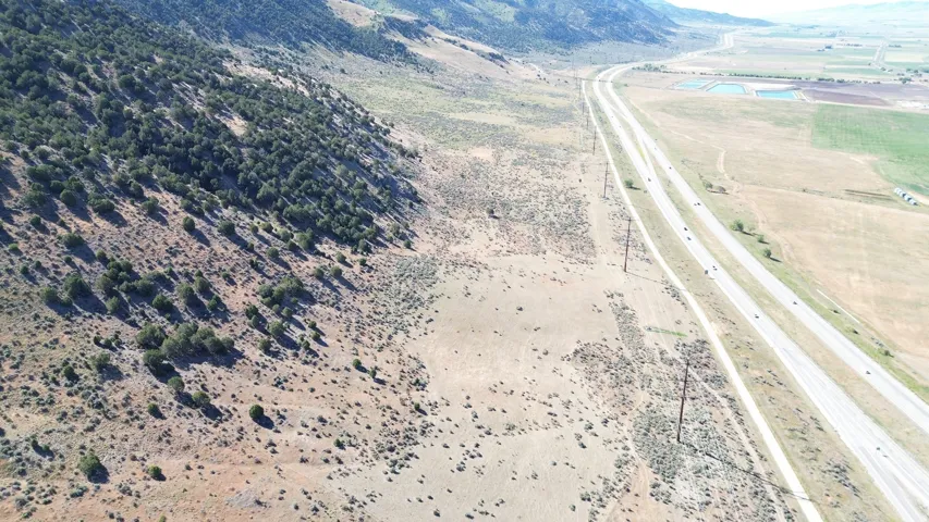 Expansive landscape featuring a multi-lane highway, distant agricultural fields, and a tree-covered hillside