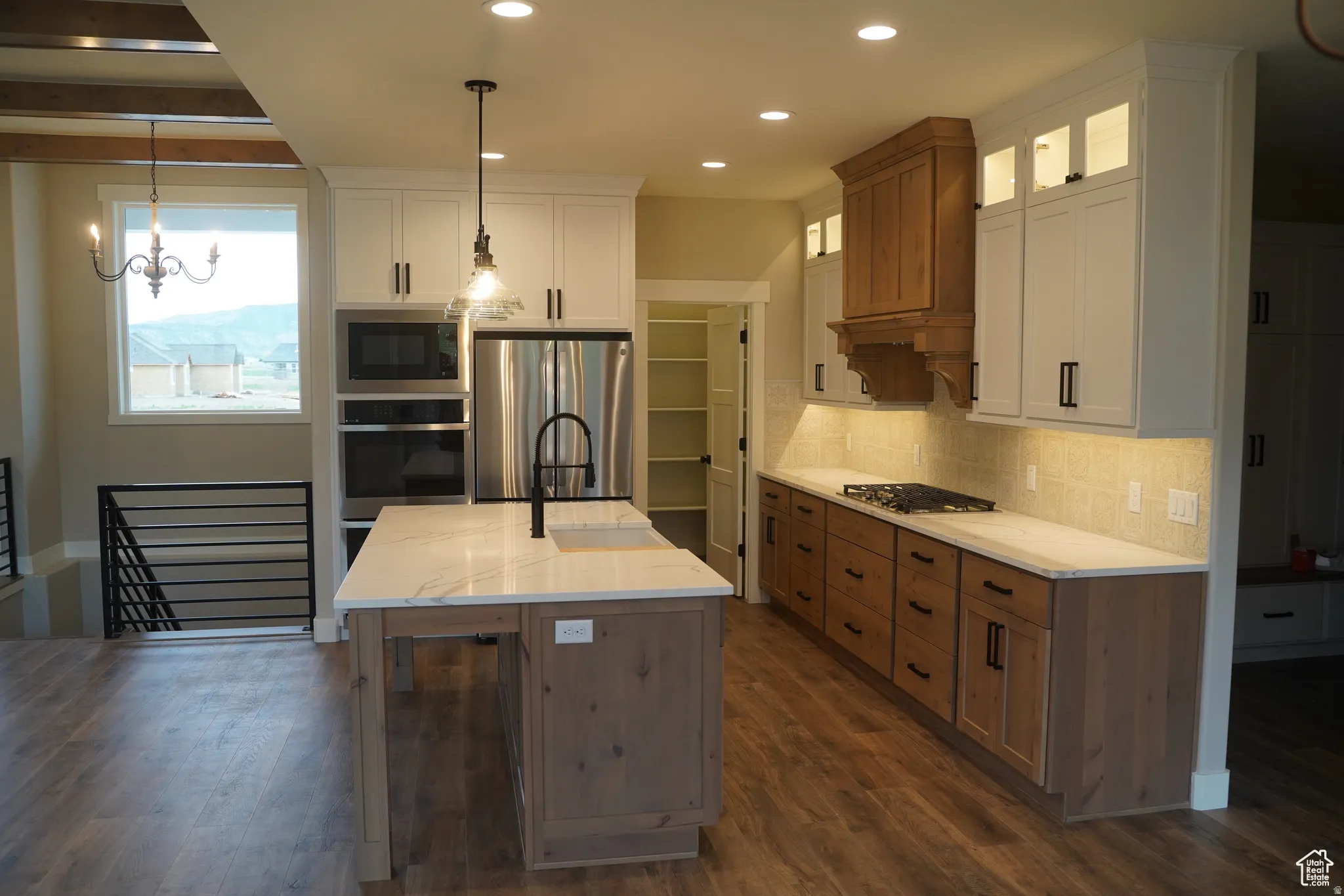 Kitchen featuring appliances with stainless steel finishes, tasteful backsplash, white cabinets, decorative light fixtures, and brown cabinetry