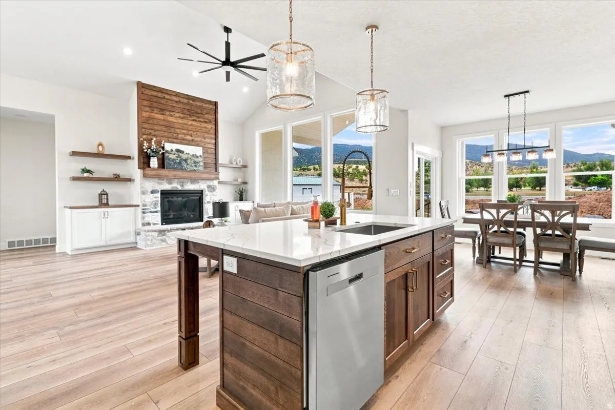 Open-concept living space featuring wood-finish flooring, a kitchen island with a white countertop, and a stone fireplace with a wood accent wall