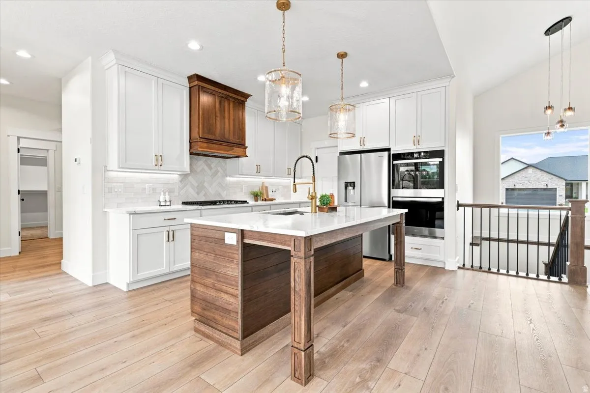 Gourmet kitchen featuring a central island with a wood-finish base, white cabinetry, integrated stainless steel appliances, and wood-finish flooring