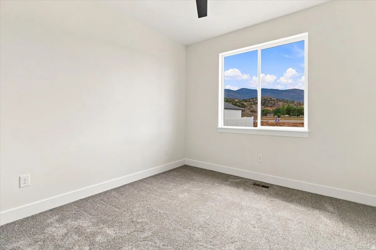 Bright room with neutral wall tones, gray carpeting, a large window, and a ceiling fan