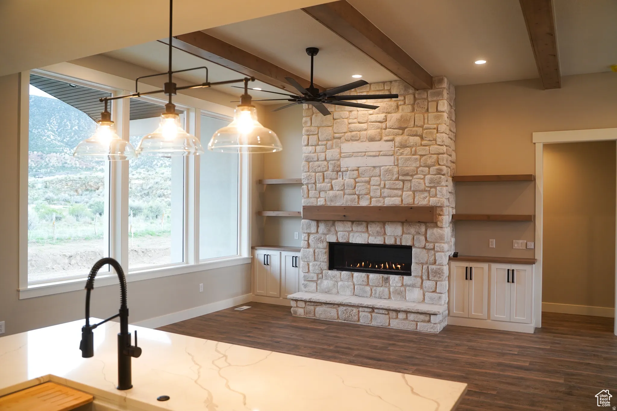 Kitchen with ceiling fan, dark wood-type flooring, a stone fireplace, light stone countertops, and beamed ceiling