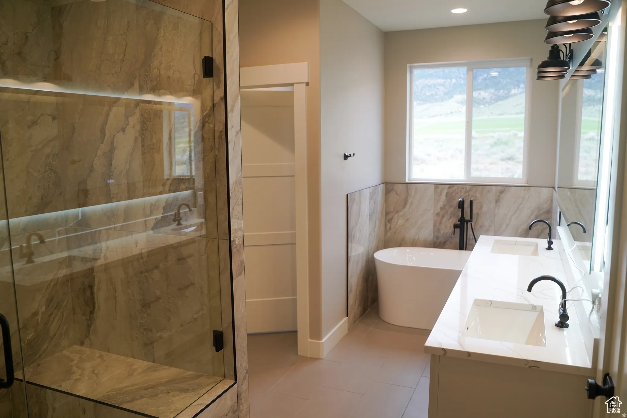 Bathroom with a marble finish shower, double vanity, a freestanding bath, light tile patterned floors, and tile walls