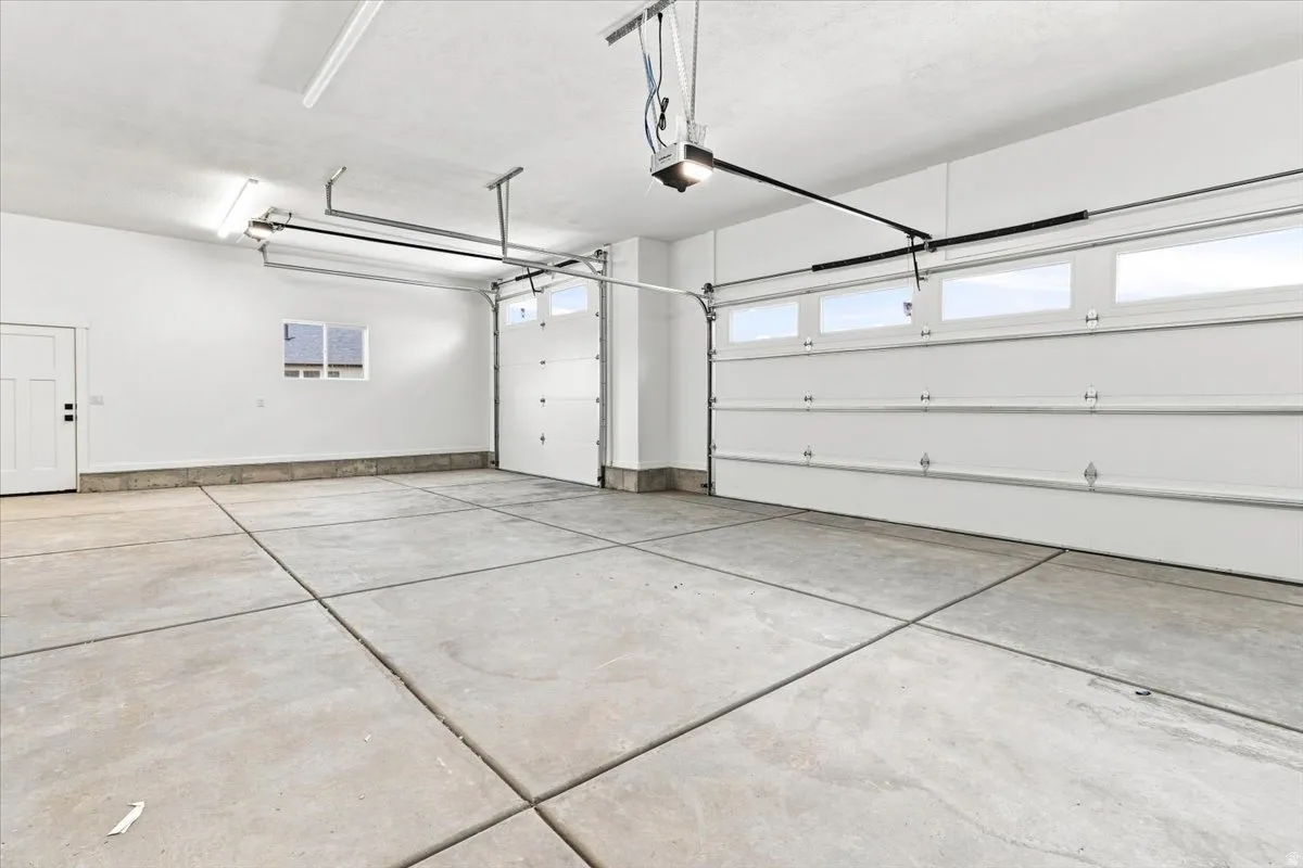 Expansive garage with concrete flooring, two overhead doors with transom windows, a side door, and a single window