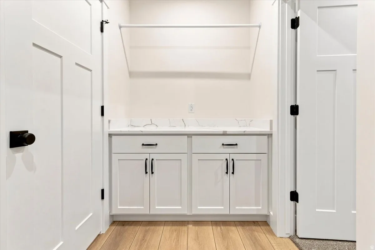 White shaker-style cabinetry with matte black hardware, a white countertop, and a clothes hanging rod