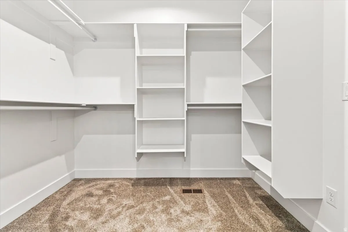 Walk-in closet with integrated shelving, multiple hanging rods, and neutral-toned carpeting