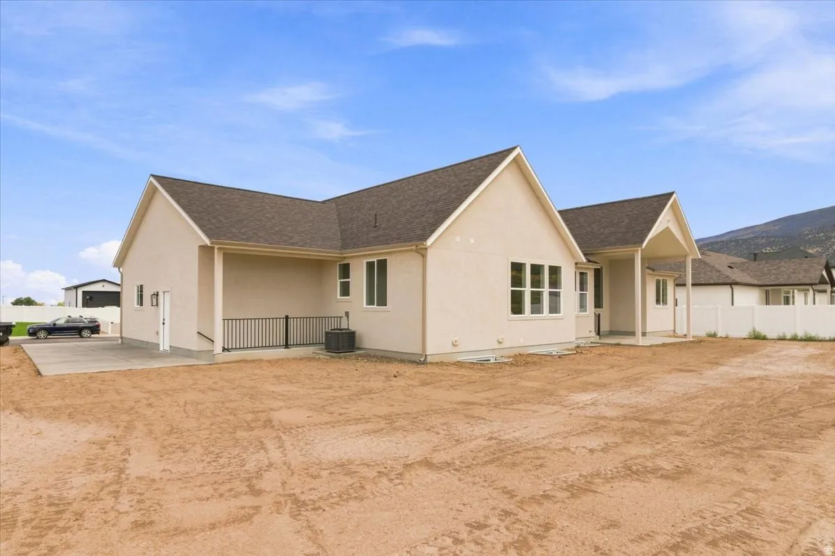 Contemporary stucco exterior, dark shingle roofing, multiple windows, covered patio, white privacy fence