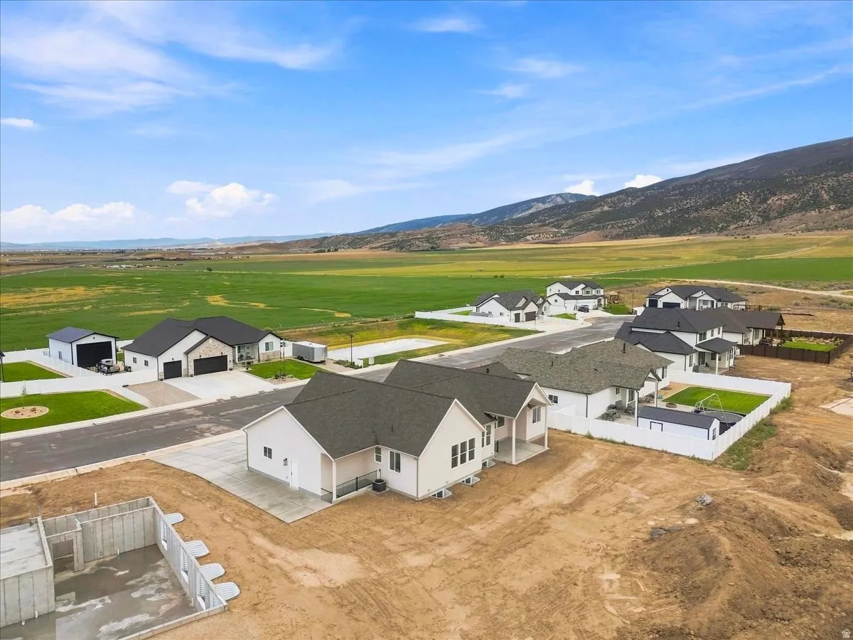 New construction homes situated in a developing community, featuring concrete driveways and surrounding open fields with distant mountains