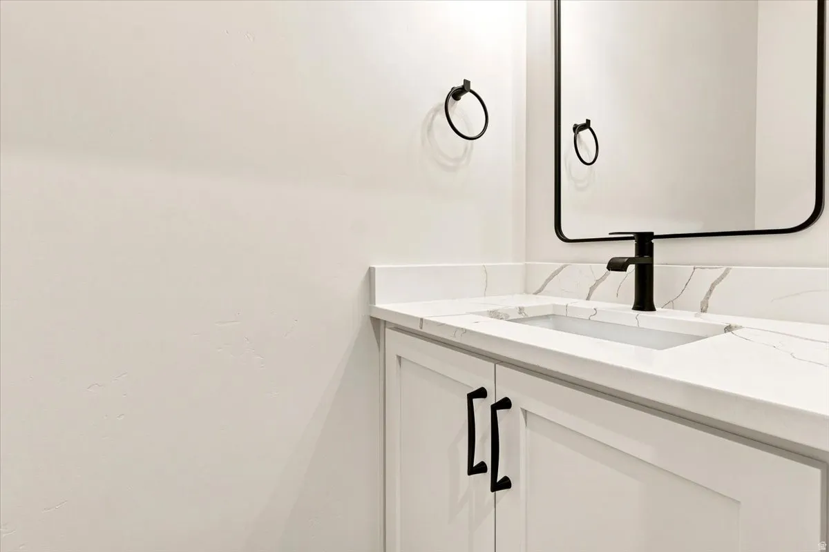 White vanity with black hardware, integrated rectangular sink, waterfall faucet, and a wall-mounted mirror