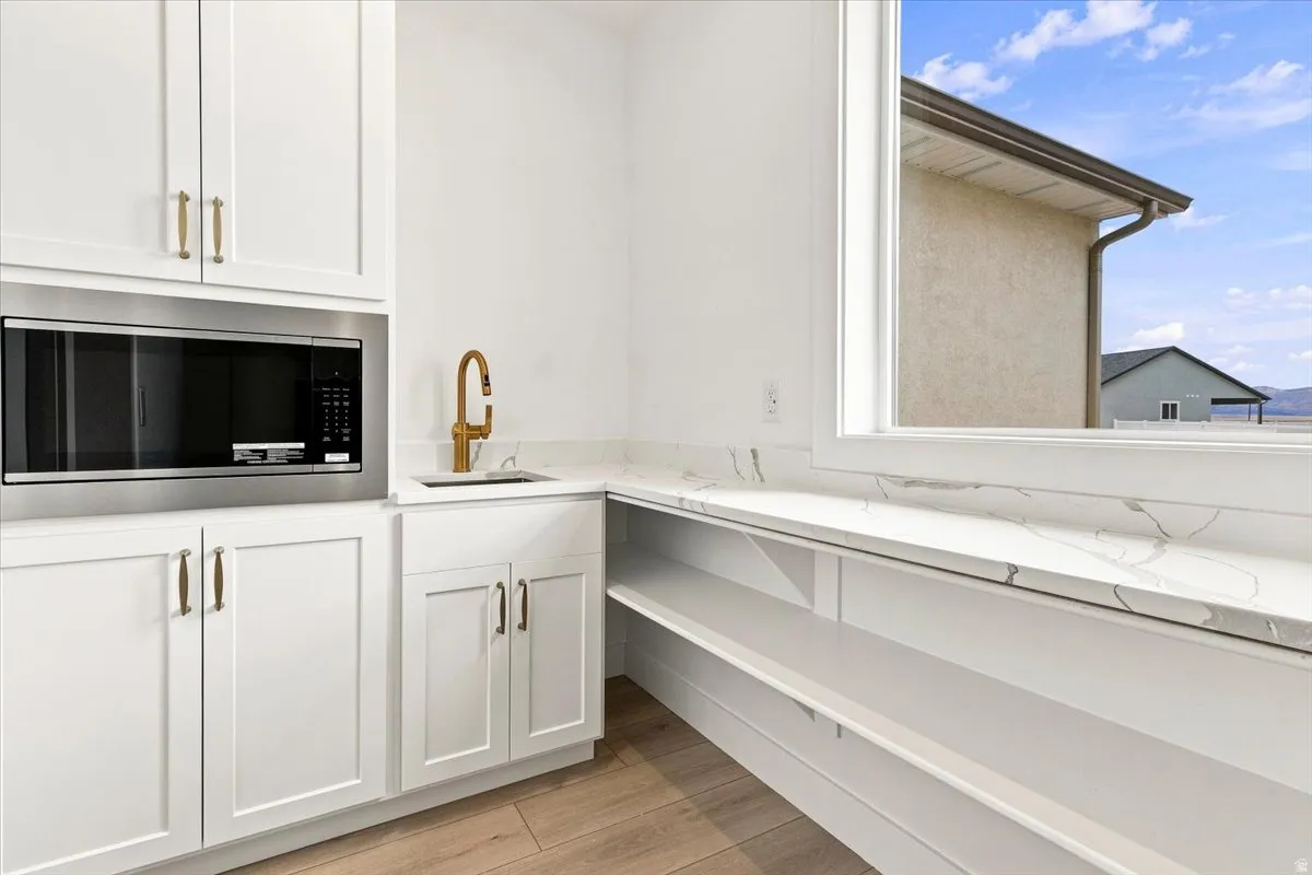 White cabinetry with gold-tone hardware, a built-in microwave, a sink with a gold-tone faucet, stone-finish countertops, and wood-finish flooring