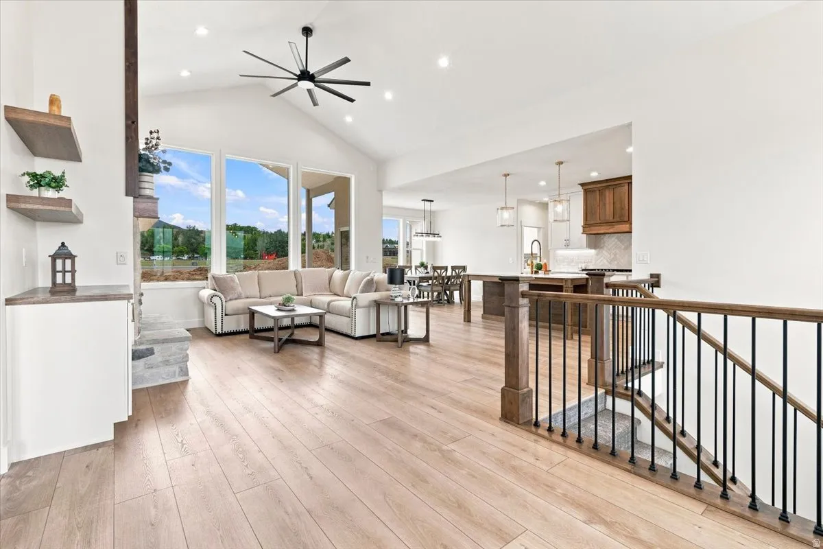 Vaulted ceiling with a modern ceiling fan, large picture windows, wood-finish flooring, built-in shelving, and a wood and iron staircase railing