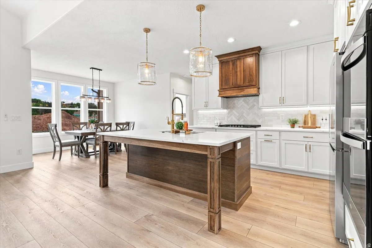 Spacious kitchen featuring an expansive center island with seating, white shaker cabinetry, a herringbone tile backsplash, wood-finish flooring, and pendant lighting