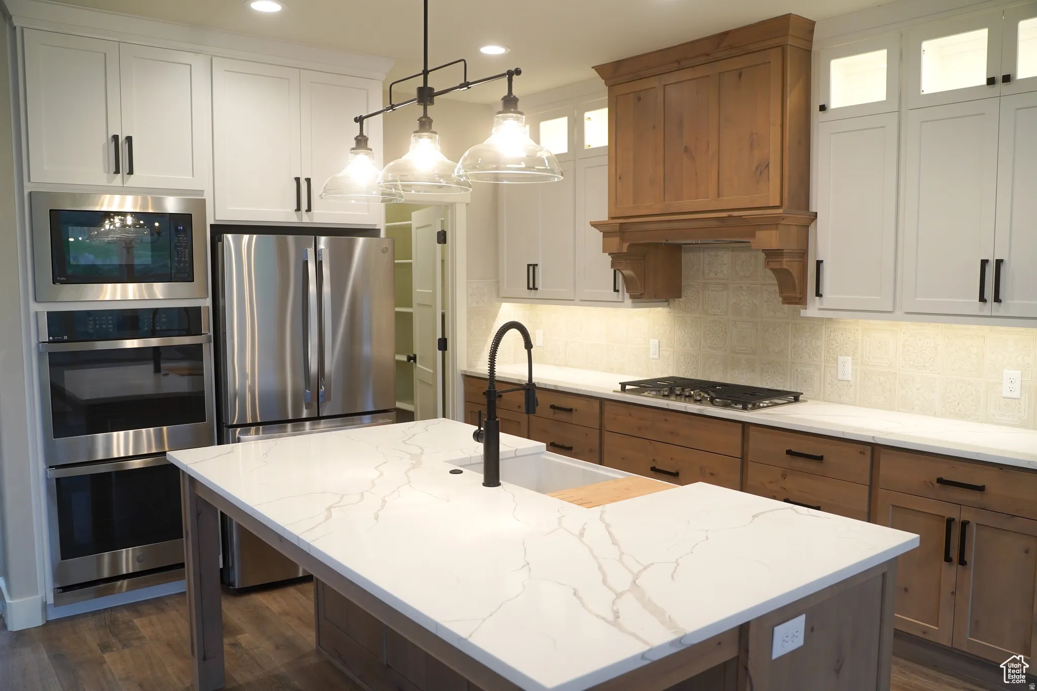 Kitchen featuring appliances with stainless steel finishes, light stone countertops, pendant lighting, an island with sink, and recessed lighting