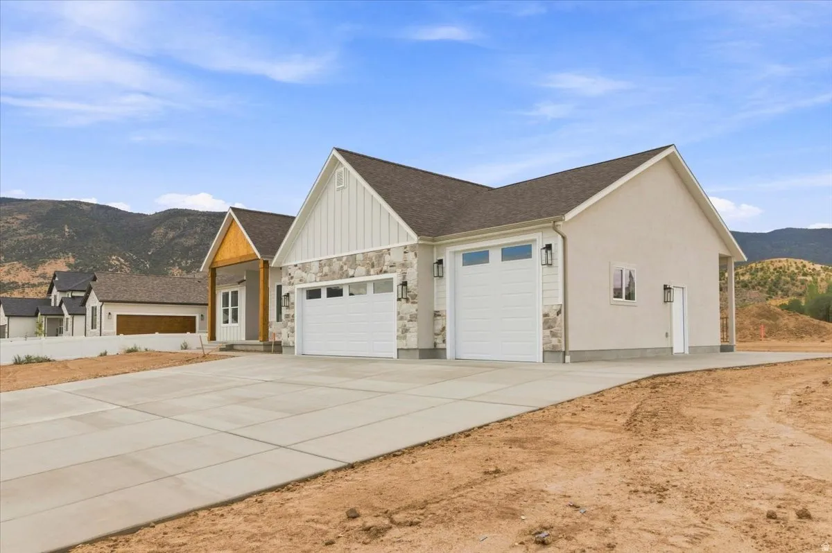 Contemporary exterior with stone and stucco accents, multiple garage bays, a covered entry with wood-finish columns, and exterior sconce lighting