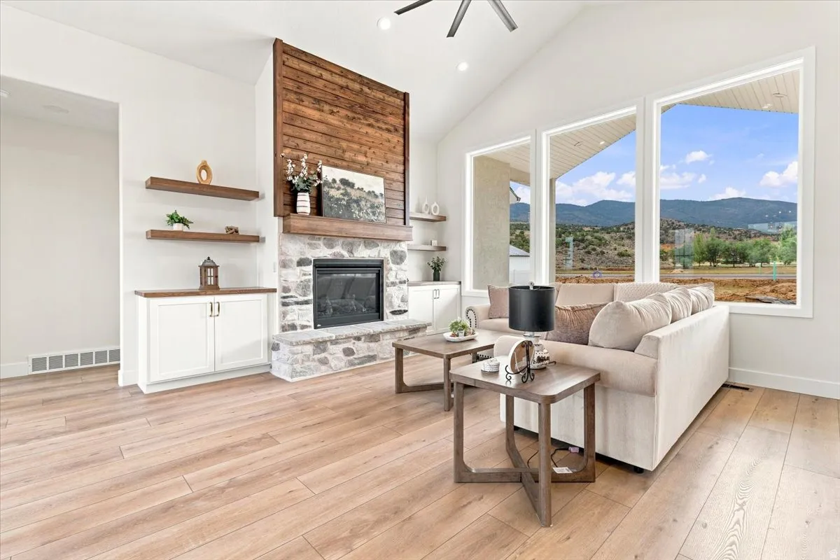 Vaulted ceiling with a ceiling fan, stone-faced fireplace with a wood mantle, wood-finish flooring, built-in cabinetry with wood countertops, and multiple large windows