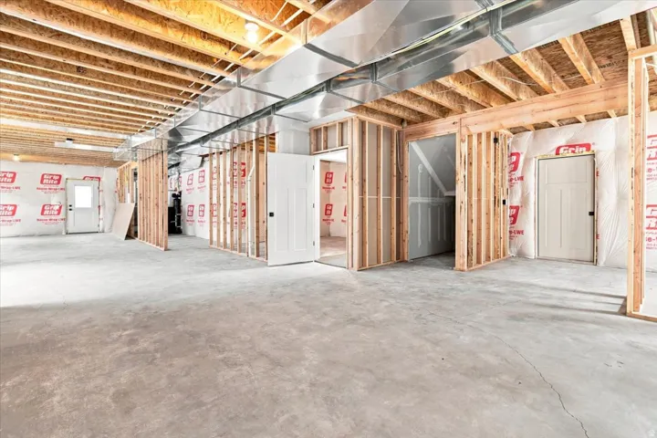 Unfinished basement with exposed wood joists, concrete flooring, framed interior walls, white panel doors, and visible ductwork