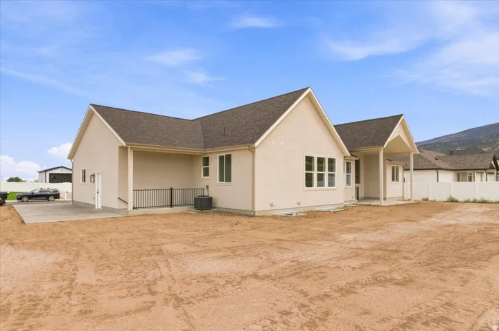 Contemporary stucco exterior, dark shingle roofing, multiple windows, covered patio, white privacy fence