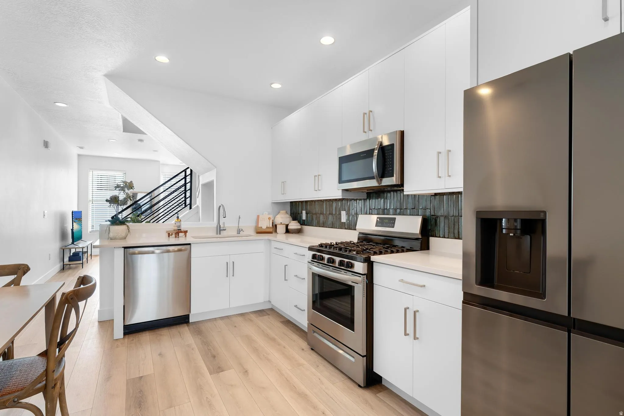 Kitchen featuring appliances with stainless steel finishes, light wood finished floors, white cabinets, a peninsula, and recessed lighting